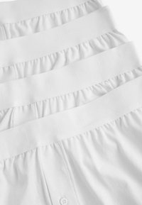 Calzoncillos de algodón blancos apilados ordenadamente, con cinturillas elásticas que presentan un logotipo en relieve y un pequeño detalle de botón en la parte frontal.