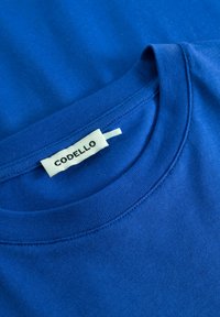T-shirt en coton bleu avec un col rond, doté d'un col cousu et d'une étiquette blanche avec "CODELLO" à l'intérieur près de l'encolure.
