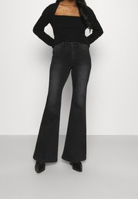 Jeans negros de campana con cintura ajustada, bolsillos frontales y una textura de denim suave, combinados con una blusa negra de punto acanalado.