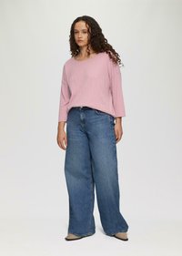 Hellrosa, gerippter Langarmoberteil kombiniert mit weit geschnittenen blauen Jeans. Das Material scheint weich zu sein, mit einem lässigen Schnitt und dezenten Texturdetails.
