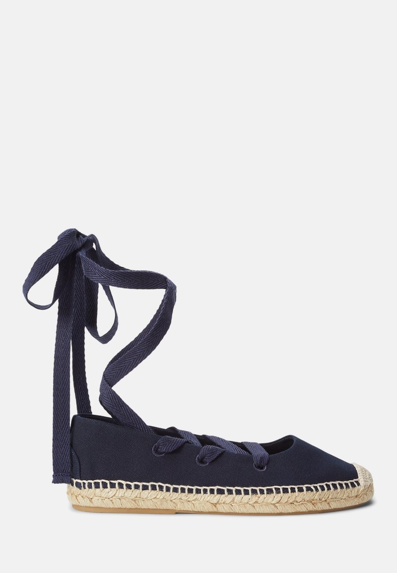 Espadrille plate bleu marine avec semelle en jute tissée et liens à nouer à la cheville sur fond blanc.