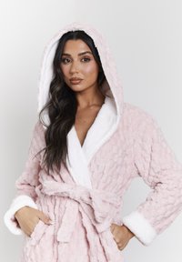 Robe cappuccio rosa realizzato in morbido tessuto con un motivo testurizzato. Presenta foderatura in soffice pile bianco, vita con cintura e due tasche laterali.