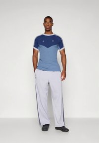 Blauw en grijs sportief T-shirt met een geometrisch ontwerp en witte accenten, gecombineerd met lichtgrijze broek met marineblauwe strepen aan de zijkant.