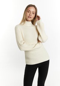 Crème ribbel turtleneck trui met lange mouwen, met een gestructureerd ontwerp en zachte textuur, gecombineerd met zwarte strakke broeken.