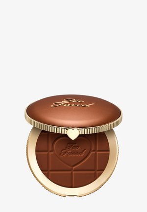Bronzener Too Faced Kompaktpuder mit herzförmig geprägt Logo und goldgerahmtem Deckel, teilweise geöffnet auf weißem Hintergrund.