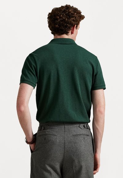 Camică polo verde cu mâneci scurte, dintr-un material texturat, cu guler ribbelat, asortată cu pantaloni gri cu bucle pentru centură și buzunare la spate.