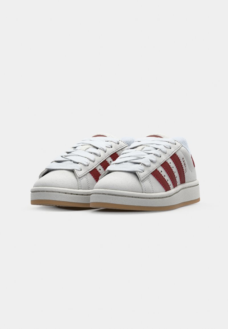 Weiße Sneaker mit roten Streifen, glattes Obermaterial, runde Zehenpartie, gepolsterte Zunge und Gummisohle. Schnürdesign, minimale Markenkennzeichnung sichtbar.