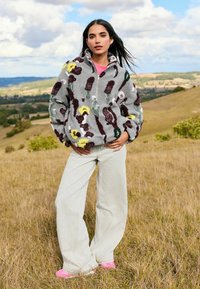 Gray fleece pullover with multicolored floral appliqués, half-zip collar, paired with light gray wide-leg pants and pink shoes.