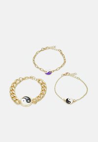 Três pulseiras douradas com pendentes de yin-yang. Uma tem uma corrente grossa, outra é uma corrente fina e delicada, e uma tem um pequeno encanto circular.