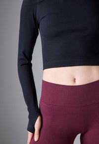 Langærmet, ribbet navy crop top parret med højtaljede bordeaux ribbede leggings, der har tommelfingerhuller i ærmerne for ekstra detaljer.