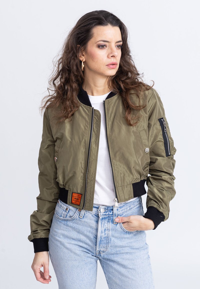 Giacca bomber verde oliva con design corto, polsini neri a coste, zip frontale e etichetta patch sulla vita.