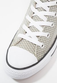 Gros plan d'une basket en mesh beige avec des lacets blancs, un embout en caoutchouc et une semelle blanche texturée.