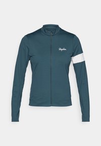 Turkusowa kurtka rowerowa z długimi rękawami, wysokim kołnierzem, pełnym zamkiem z przodu, białą wstawką na rękawie oraz logo Rapha na klatce piersiowej.