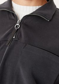Giubbotto nero con zip e colletto strutturato, dotato di una zip a mezza lunghezza, tasche frontali e un tessuto liscio e testurizzato.