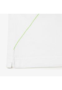 Prenda blanca con tela texturada, que presenta un detalle de costura en zigzag verde brillante a lo largo del dobladillo y la abertura lateral.