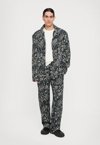 Set de jachetă și pantaloni cu imprimeu floral închis, confecționat dintr-un material texturat, având un croi lejer, guler larg și un tricou alb în contrast dedesubt.