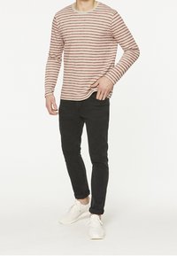 Pitkähiha odottavassa t-paidassa, jossa on vaaleanpunaisia ja kermanvärisiä raitoja, yhdistetty mustiin slim-fit-farkkuihin ja valkoisiin lenkkareihin. Yksinkertainen pyöreä pääntie, rento istuvuus.