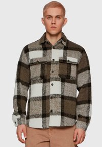 Plaid shirt featuring large brown and white checks, made of textured fabric, with two chest pockets and brown buttons, featuring a collar.