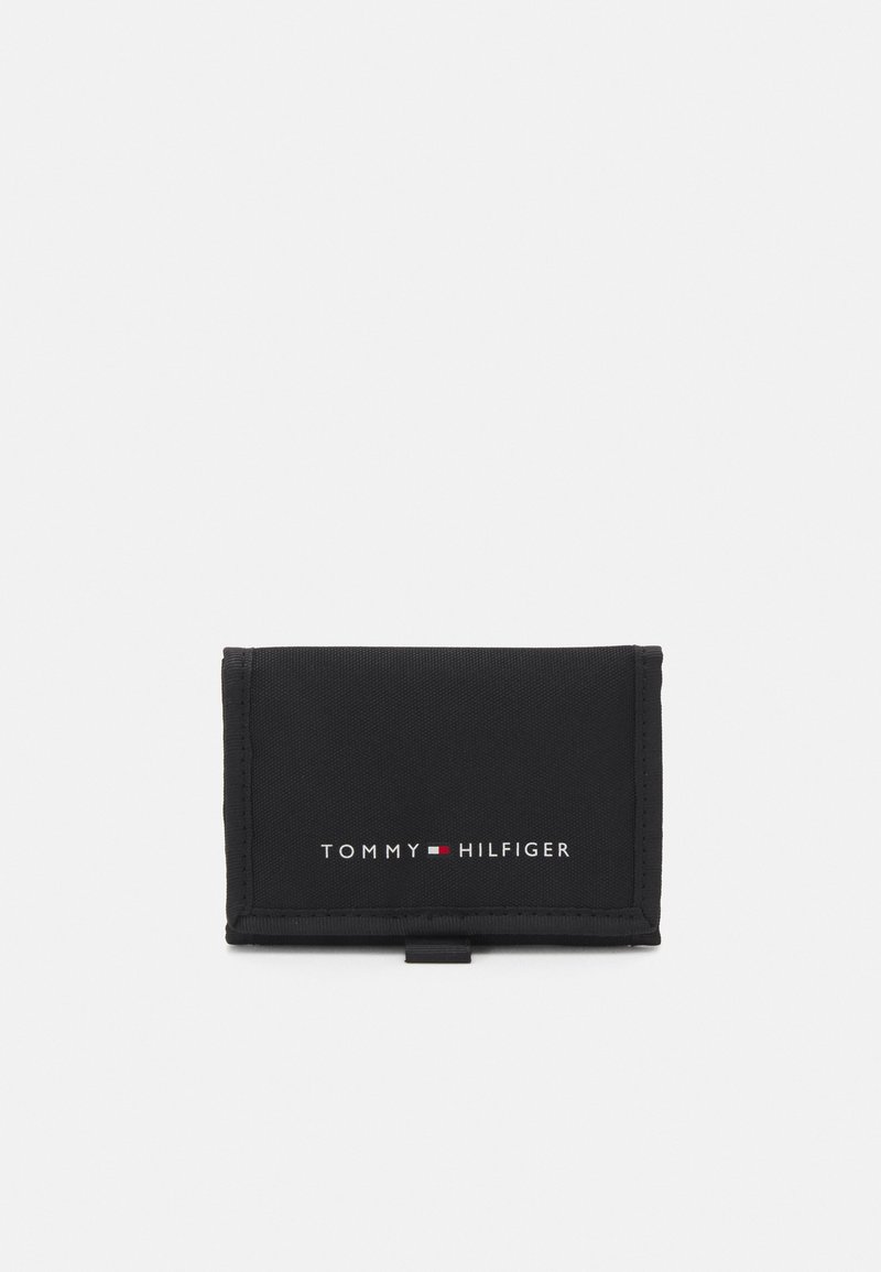 Black fabric wallet with a fold-over design. Features white "TOMMY HILFIGER" logo with red and white accents. Smooth texture and compact shape.