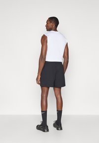 Λευκό αμάνικο μπλουζάκι, μαύρα σορτς, μαύρες κάλτσες με λευκό λογότυπο, μαύρα αθλητικά παπούτσια. Η φιγούρα είναι στραμμένη μακριά από τον θεατή.