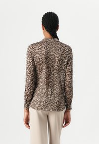 Leopardmønstret bluse med lange ærmer, gennemsigtigt stof, subtil krave og afrundet kant, parret med kridhvide bukser.