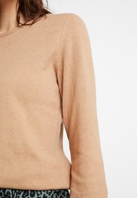 Maglione beige chiaro realizzato in tessuto morbido, con scollo rotondo e maniche lunghe, dotato di una texture liscia e di una vestibilità aderente.
