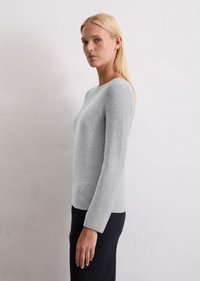Jasnoszara, długosleeve sweter z okrągłym dekoltem i teksturowanym wzorem dzianiny; zestawiony z ciemną spódnicą, na neutralnym tle.