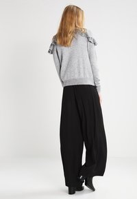 Grauer Pullover mit Rüschendetail an der Schulter, kombiniert mit weiten schwarzen Hosen. Der Pullover hat einen gerippten Saum; die Hose ist weit und fließend.