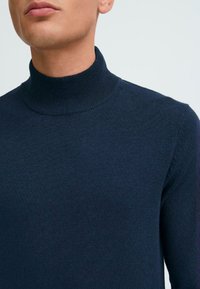 Pulover cu guler înalt de culoare bleumarin, fabricat dintr-un material moale, cu un guler ribat și o textură netedă. Vedere detaliată asupra gulerului.