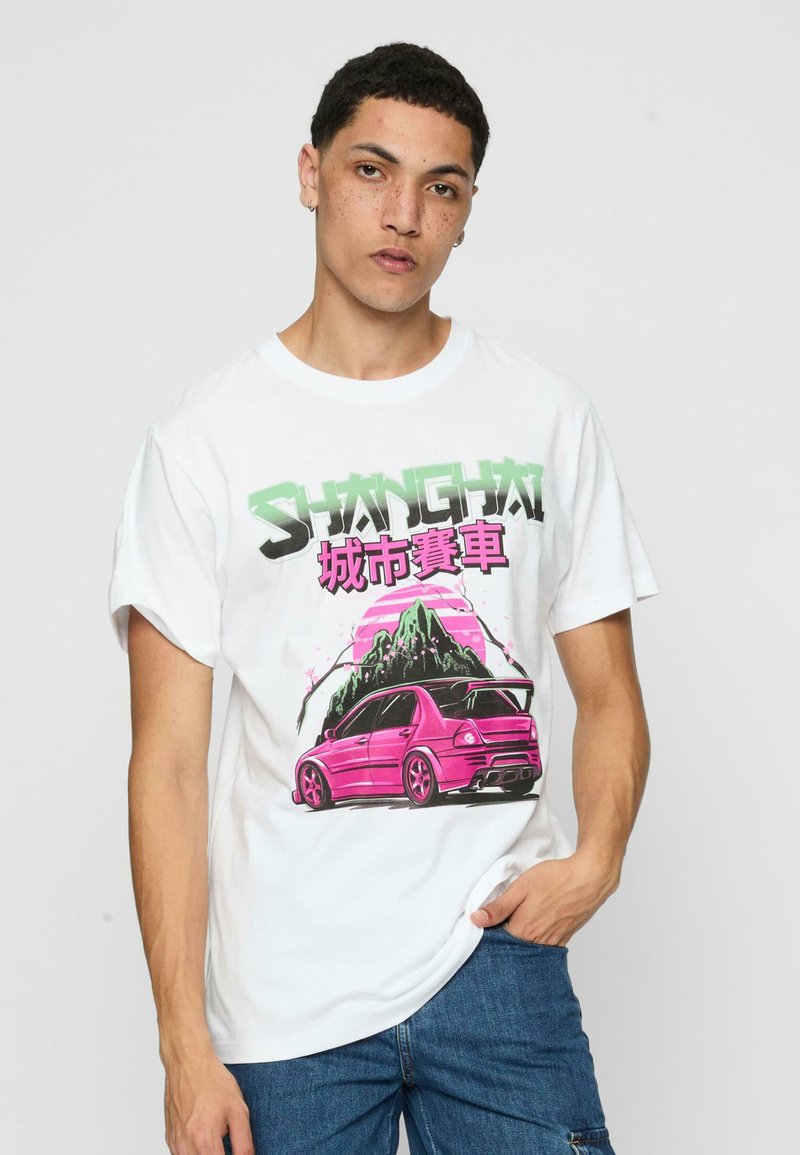 Fehér pamut póló, rózsaszín autó és hegyek grafikai tervezetével, zöld és rózsaszín "SHANGHAI" felirattal. Lazán illeszkedő fazon.