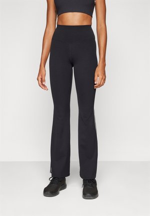 Zwart slim-fit yoga broek met wijde pijpen en hoge tailleband, gedragen met een zwarte sportbeha en zwarte sportschoenen op een model.
