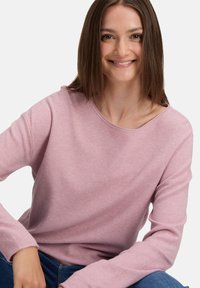 Helle rosa langärmlige Pullover mit lockerer Passform. Rundhalsausschnitt und strukturierter Strickstoff, kombiniert mit blauen Jeans.