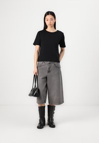 T-shirt noire à manches courtes associé à des culottes en denim gris, des bottes noires jusqu'aux genoux et un petit sac à main noir. Design simple et couleurs discrètes.