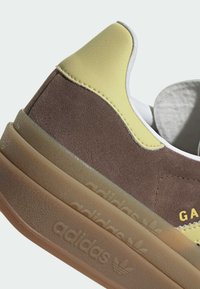 Close-up of brown suede Adidas sneaker heel with yellow leather accent and translucent gum sole embossed with Adidas logo.