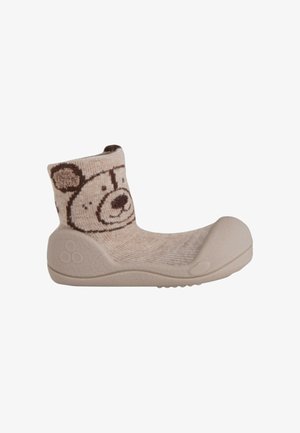 Calzino-scarpa beige per bambino con suola in gomma e un volto di orso sorridente lavorato a maglia sul polsino della caviglia.