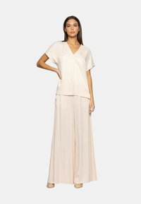 Completo a due pezzi composto da una maglietta rosa chiaro a maniche corte con scollo a V e pantaloni ampia coordinati in un tessuto fluido. Texture liscia.