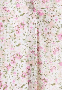 Blumenhemd mit Knopfleiste, das einen weißen Hintergrund mit rosa und grünen Mustern zeigt. Es hat runde Kunststoffknöpfe entlang der Vorderseite.