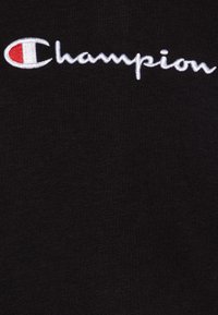Tejido de algodón negro con un logo bordado en blanco que dice "Champion" con un acento rojo en el lado izquierdo. Textura suave, sin patrones.