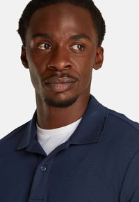 Polo de manga corta en color navy, elaborado con un tejido texturizado, que cuenta con un collar plano, una tapeta de botones y una sutil marca en el hombro.