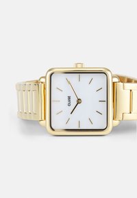 Square gold watch with a white face, accented by slender gold hands and markers, featuring a metal link bracelet. Brand name: CLUSE.