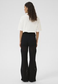 Witte oversized t-shirt gecombineerd met hooggewaisted zwarte wijde broek met een getextureerd, open gebreid ontwerp en diagonaal patroon.