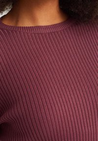 Ribbed knit sweater in deep burgundy, featuring a crew neck design and smooth texture, highlighting vertical rib patterns.