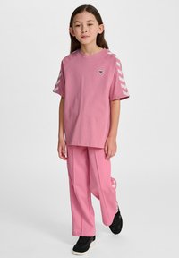 Lyserød bomulds T-shirt med korte ærmer, der har skulderstriber og et lille logo. Sættet er stylet med matchende lyserøde bukser og sorte sneakers.