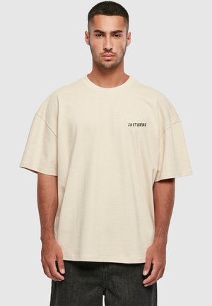 Beige oversized t-shirt lavet af blød bomuld med rund hals, korte ærmer og et lille trykt logo på venstre bryst.