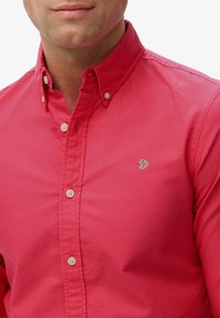 Czerwona koszula zapinana na guziki z kołnierzykiem, z małym nadrukowanym logo na piersi. Wykonana z fakturowanej tkaniny z widocznymi guzikami.