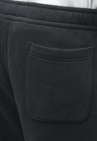 Crne dukserice s teksturiranim materijalom, elastičnom strukom i jednom stražnjom džepnom patch-om sa šivanim rubovima.