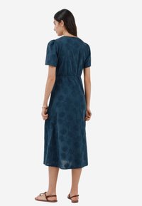 Abito in cotone di colore blu scuro con maniche a sbuffo corte, vita cinched e motivo floreale in rilievo. Lunghezza alla caviglia con vestibilità rilassata.