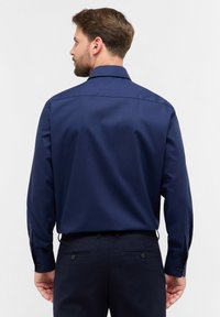 Camicia a maniche lunghe blu navy in tessuto liscio, con colletto classico, polsi con bottoni e una vestibilità sartoriale, caratterizzata da un design posteriore semplice.