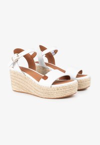 Sandalias de cuña blancas con una plataforma de yute estilo espadrille, que presentan dos correas anchas y una hebilla ajustable en el tobillo. Textura de cuero suave.