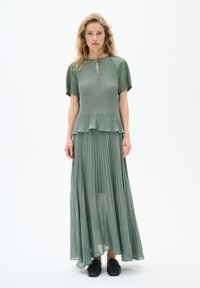 Grünes, plissiertes Maxikleid mit kurzen Ärmeln, Schlüssellochausschnitt und mehrlagigen Rüschen an der Taille; aus leichtem Stoff gefertigt.